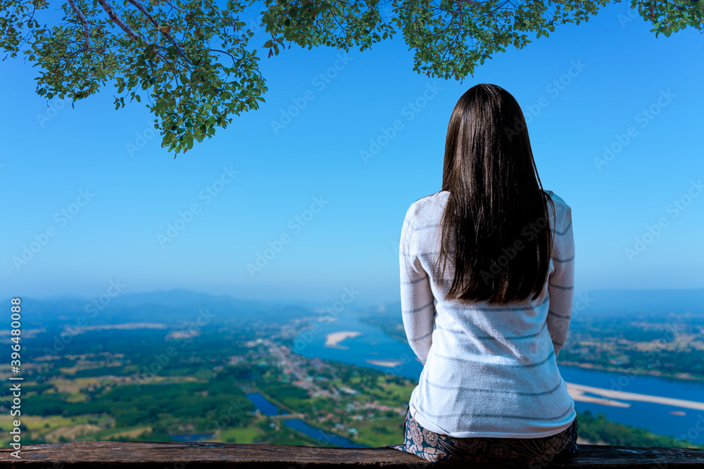 Young traveler woman is sitting looking at the river and sky with mountains natural background.