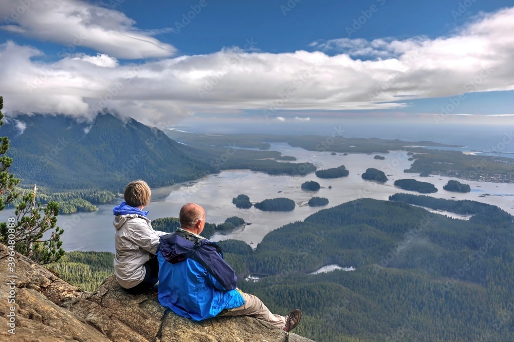 Fototapeta premium Two friends on cliff above the ocean with many little islands. Vancouver Island. Tofino. British Columbia. Canada