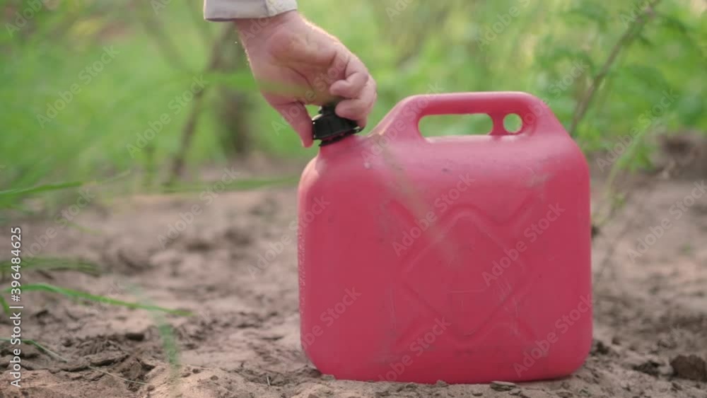 A man unscrews the lid of a red plastic canister A man unscrews the lid of a red plastic canister