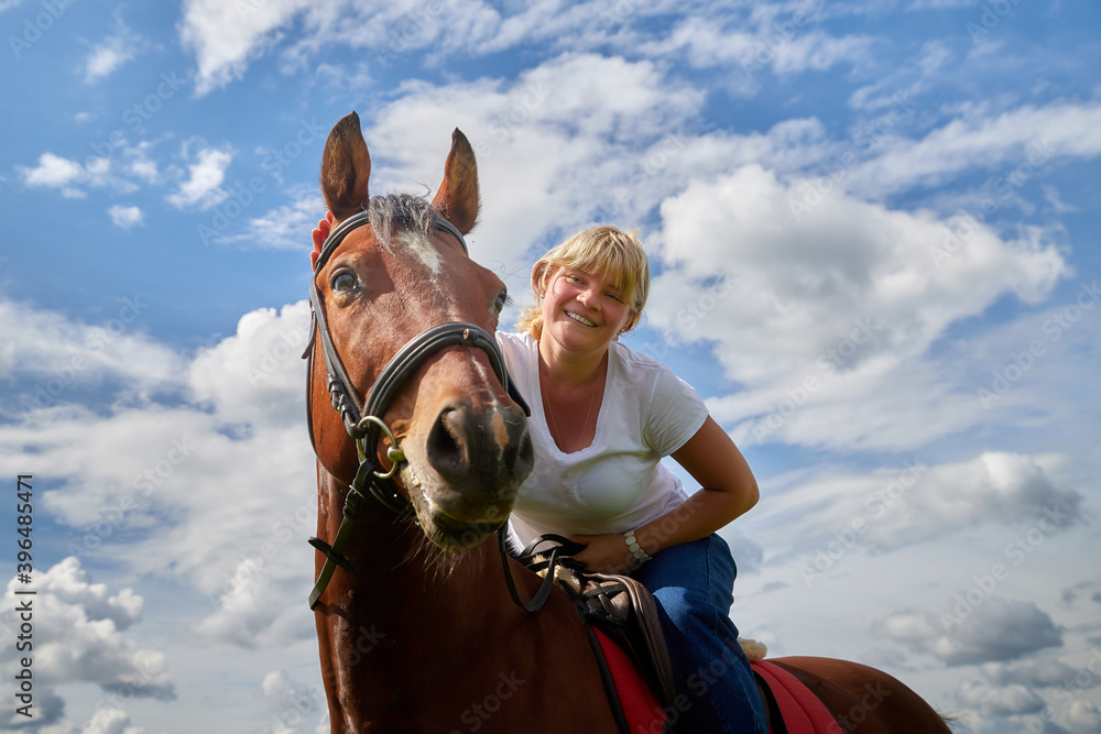 Obraz premium Girl riding on a horse on a green field and a blue sky with white clouds on the background