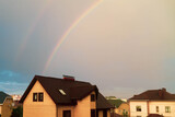Roofs of private houses after rain, dark sky, rainbow in the sky.