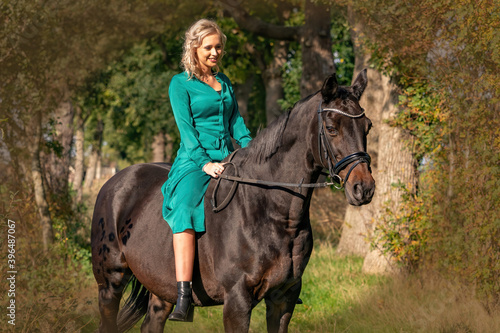 Portrait of a blonde girl in a vintage green dress with a big skirt posing with a brown horse. Selective focus