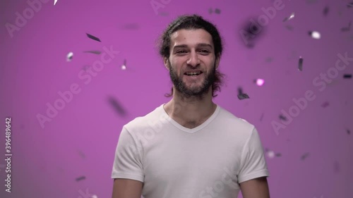 shiny confetti falls from above on a pink background on a brutal guy with brody in a white t-shirt. He smiles and enjoys the holiday and magic. High quality FullHD footage photo