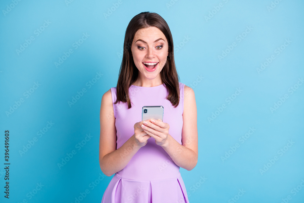 Phot of amazed positive young lady wear purple outfit hold smartphone novelty isolated on blue color background Phot of amazed positive young lady wear purple outfit hold smartphone novelty isolated on blue color background
