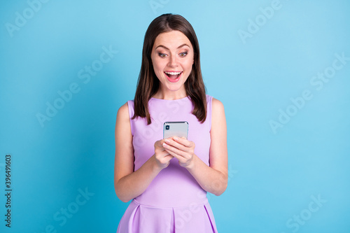 Phot of amazed positive young lady wear purple outfit hold smartphone novelty isolated on blue color background