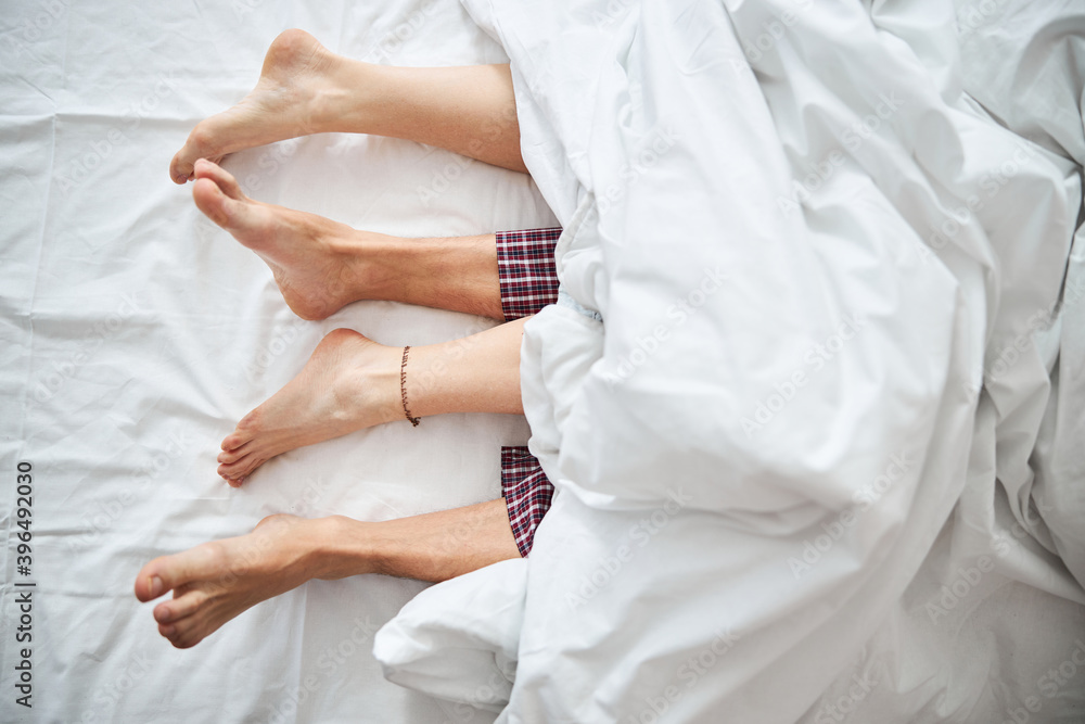 Obraz premium Loving young couple with bare feet lying in bed