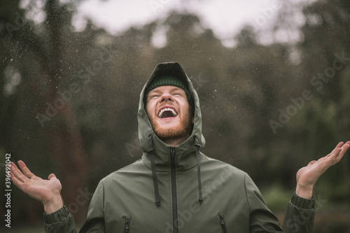 Foto Young man in a green coat standing in the rain and smiling