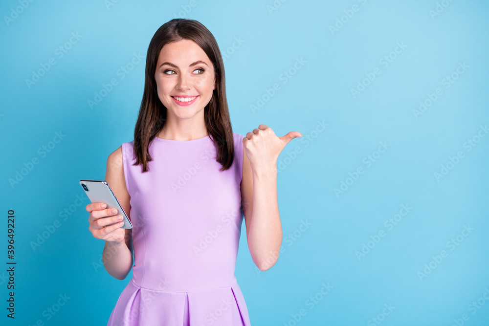 Photo of beautiful brown haired woman look point empty space hold smartphone isolated on blue color background Photo of beautiful brown haired woman look point empty space hold smartphone isolated on blue color background