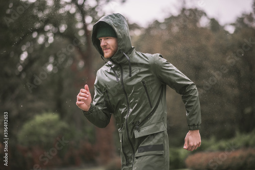 Young bearded man in a hood running under the rain