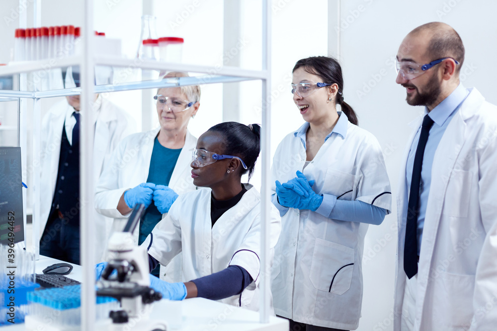 Team of scientists with diverse ethnicity analysing virus patology in modern facility. African healthcare researcher in biochemistry laboratory wearing sterile equipment. Team of scientists with diverse ethnicity analysing virus patology in modern facility. African healthcare researcher in biochemistry laboratory wearing sterile equipment.