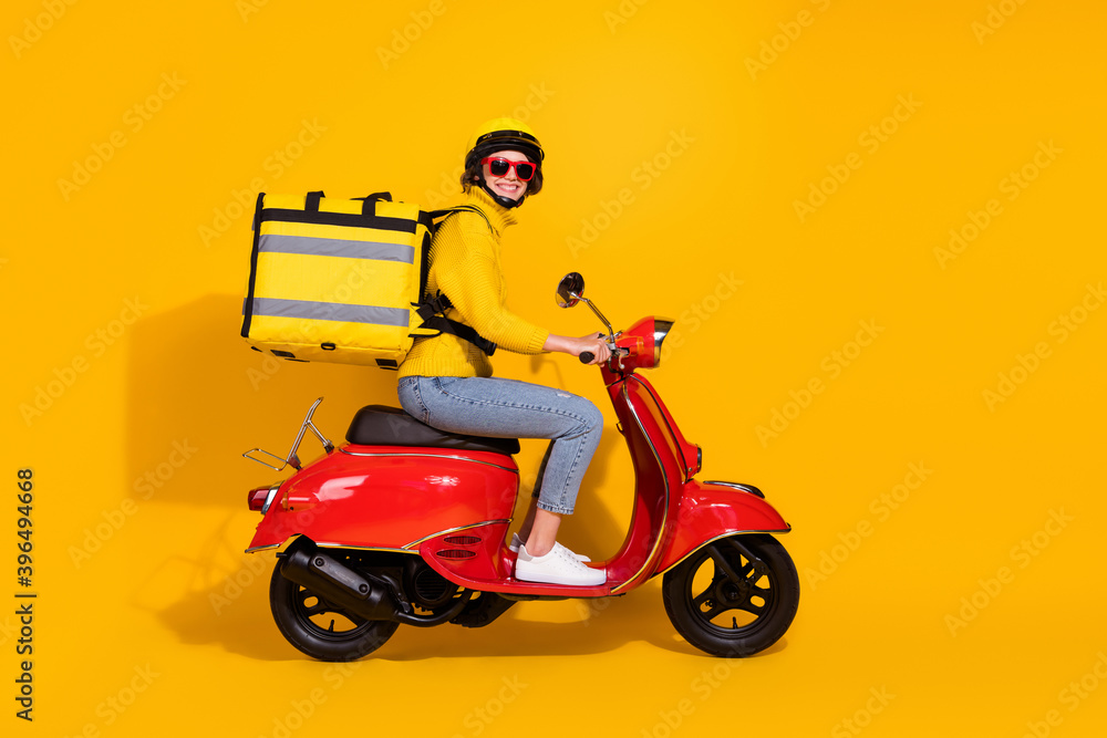 Photo portrait of courier woman delivering big yellow package driving red retro scooter isolated on vivid yellow colored background Photo portrait of courier woman delivering big yellow package driving red retro scooter isolated on vivid yellow colored background