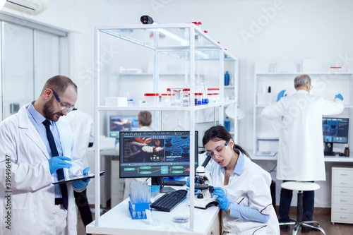 Young scientists with tablet pc and microscope making tests in busy lab. Team of researchers doing pharmacology engineering in sterile laboratory for healthcare industry with african assistant in the