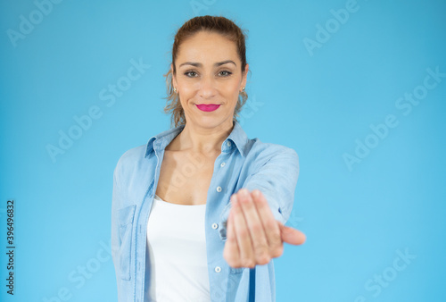 Young woman on blue background inviting to come with hand. Happy that you came