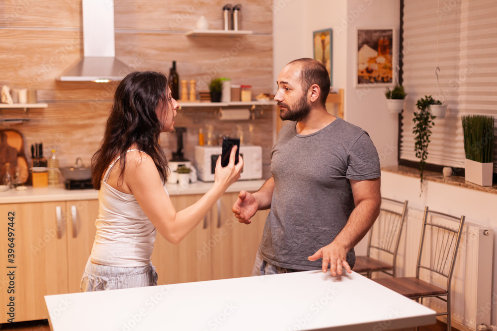 Woman looking disappointed at husband after catching him cheating while holding phone. Heated angry frustrated offended irritated accusing her man of infidelity showing him messages . Woman looking disappointed at husband after catching him cheating while holding phone. Heated angry frustrated offended irritated accusing her man of infidelity showing him messages .