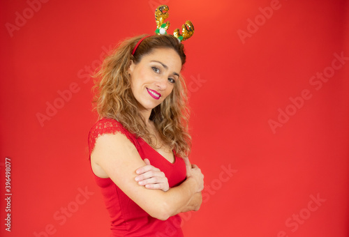 Young beautiful woman with curly hair wearing christmas headband standing on red background happy face smiling with crossed arms looking at the camera. Positive person.