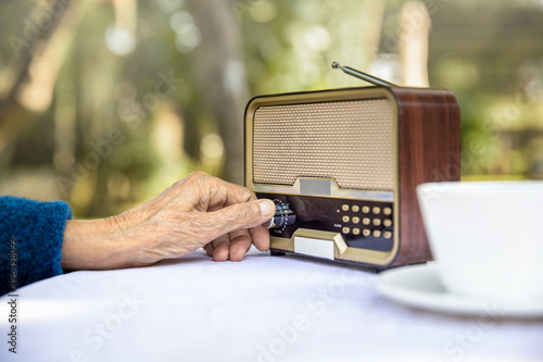 Murais de parede Senior woman hand turning knob on vintage radio in backyard.