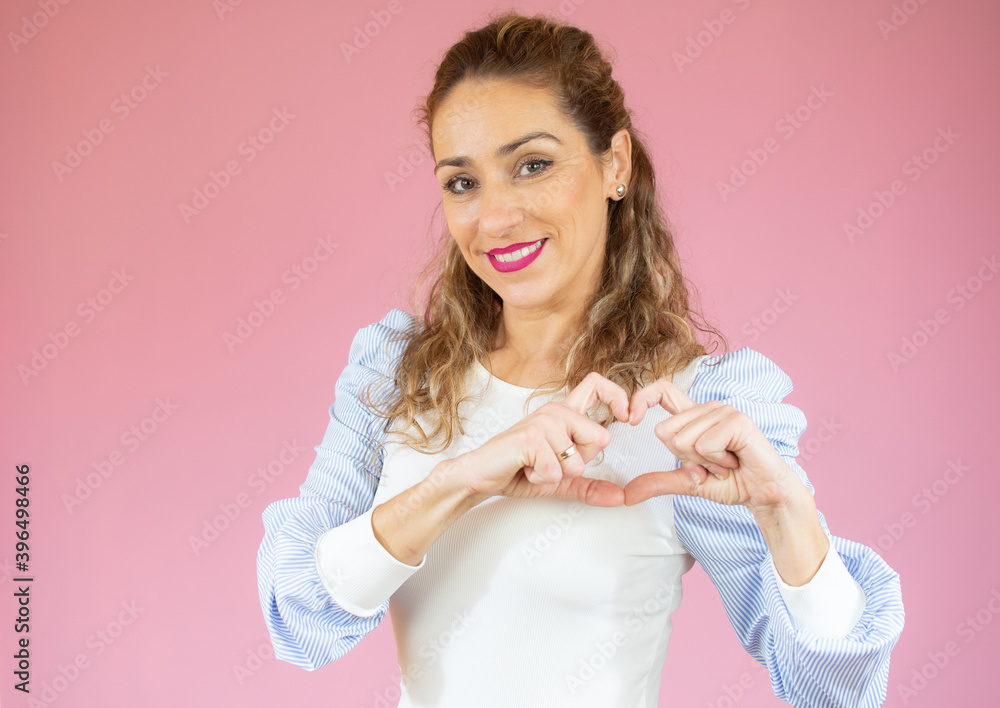 Portrait of young, pretty woman in casual shirt showing with her finger heart figure, sending love to her lover, standing over pink background Portrait of young, pretty woman in casual shirt showing with her finger heart figure, sending love to her lover, standing over pink background