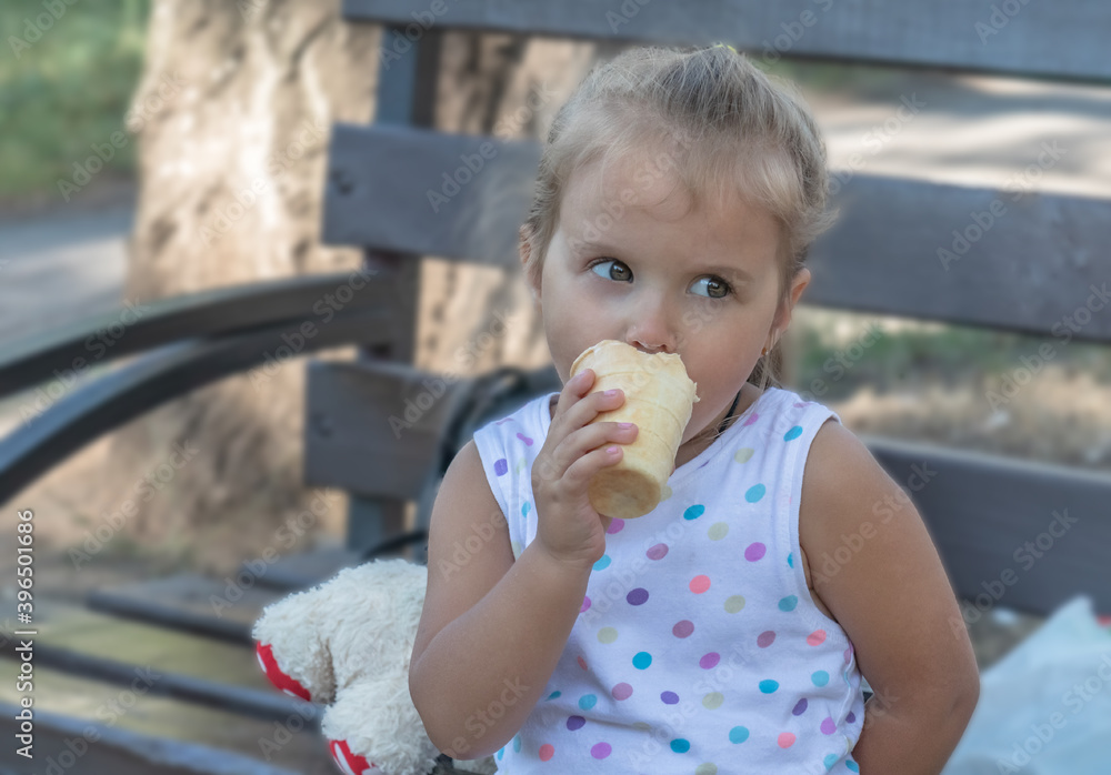 A child three-year-old girl with big eyes, blonde, sits on a bench and eats ice cream A child three-year-old girl with big eyes, blonde, sits on a bench and eats ice cream