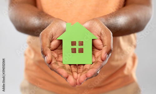 eco living, environment and sustainability concept - close up of young african american man holding green house icon over grey background