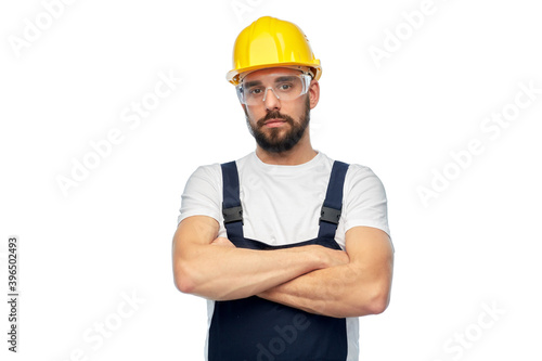 profession, construction and building - male worker or builder in yellow helmet and goggles with crossed arms over white background © Syda Productions