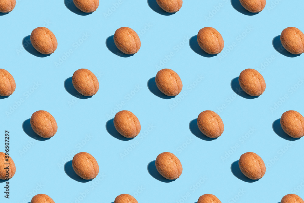 Seamless regular pattern with walnuts on a light blue background. Hard light. The concept of vegetarianism and proper nutrition. Seamless regular pattern with walnuts on a light blue background. Hard light. The concept of vegetarianism and proper nutrition.