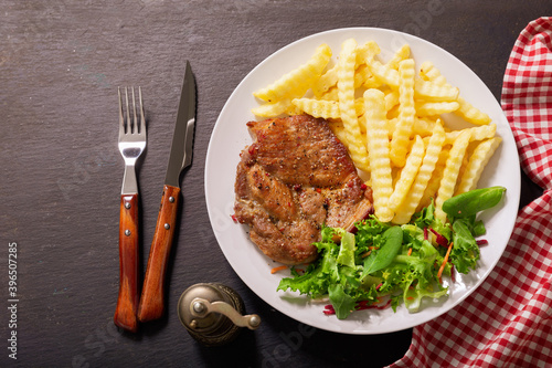 plate of grilled pork with french fries and salad on a dark background