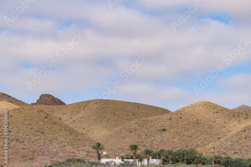 Oasis in the desert between mountains with little white house in the center blue sky with clouds.