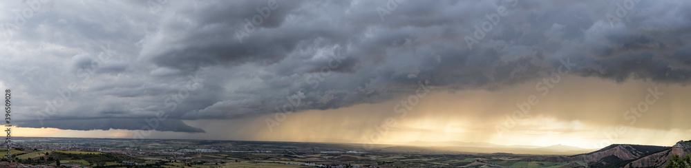 Purple storm clouds with rain in the background and sunset sky over green fields.