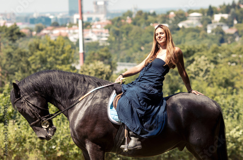 Girl with a long copper hair and long flowy shoulderless dress,  ride a black horse with trees in the background.