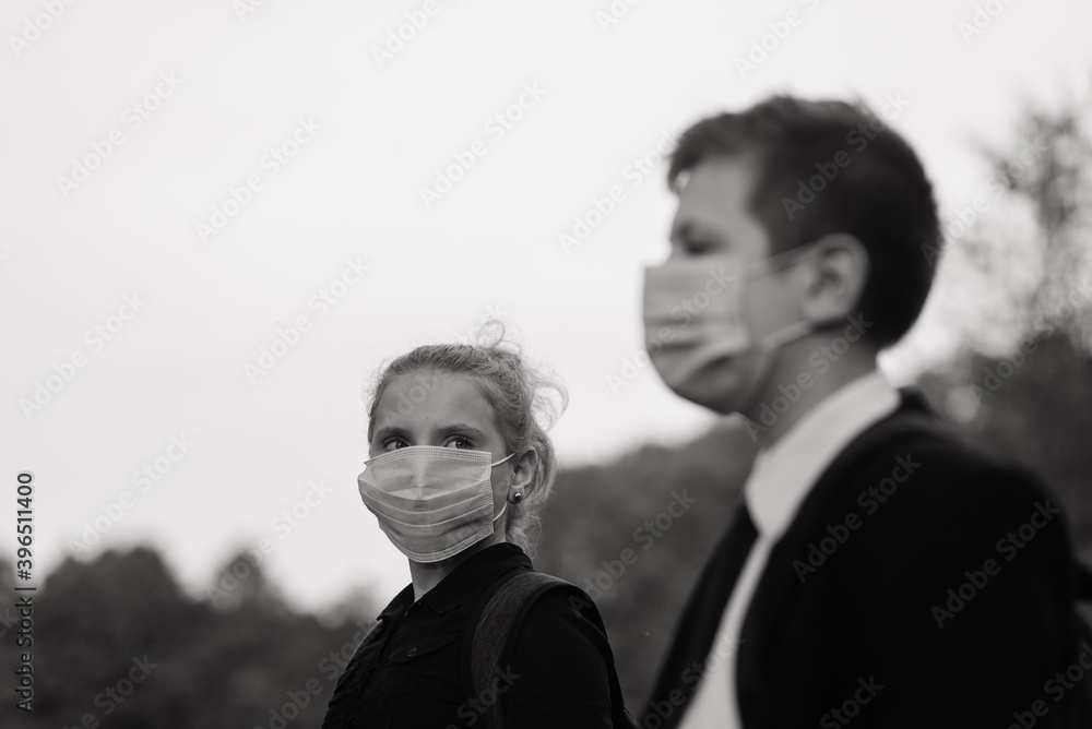 Schoolchildren, a boy and girl in medical masks walk in the city park. Schoolchildren, a boy and girl in medical masks walk in the city park.