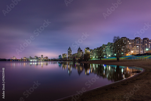 Night view of modern buildings in the Obolon district of Kiev  Ukraine  close to the Dnieper River  The lights reflect on the calm water.