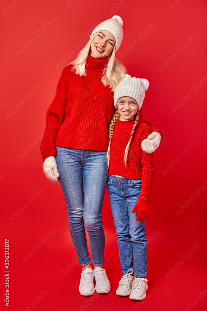 Fototapeta premium mother woman and child girl in warm clothes posing at camera, full-length portrait, isolated on red studio background