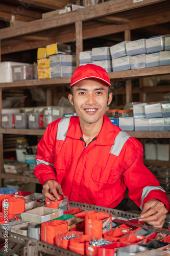 young mechanic smiled at the camera in wearpack and hat looking for parts on the spare parts rack photo