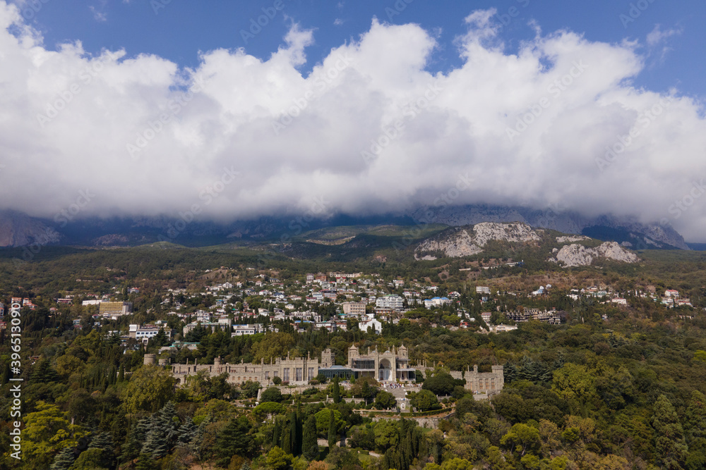 Aerial drone photo of Vorontsov palace, huge green famous garden against the mountains hidden in fog in sunny day, sightseeing in the Crimea