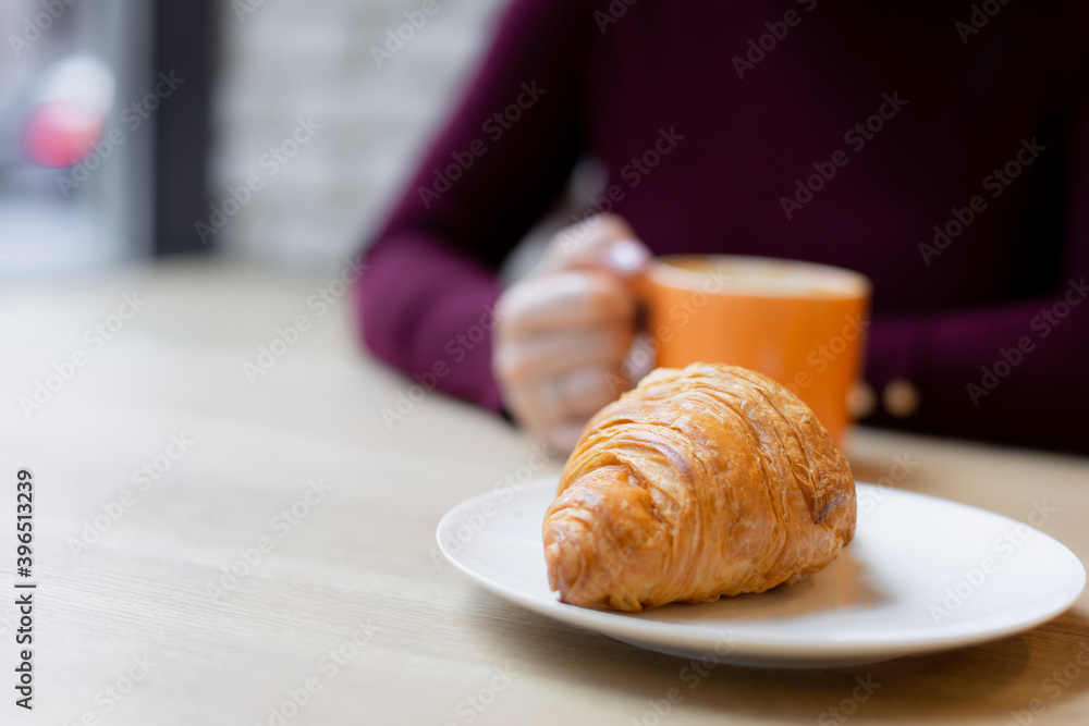 A girl has a croissant for Breakfast in a cafe
