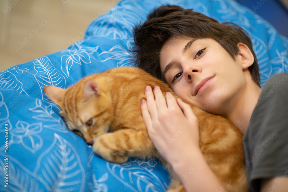 Funny young red tabby cat sleeps together with teen boy in bed at home Funny young red tabby cat sleeps together with teen boy in bed at home