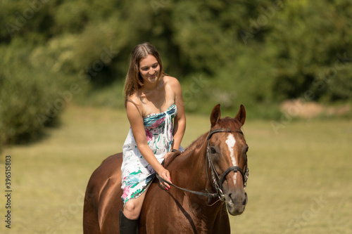 Girl with a long brown hair and tall boots rides a horse.