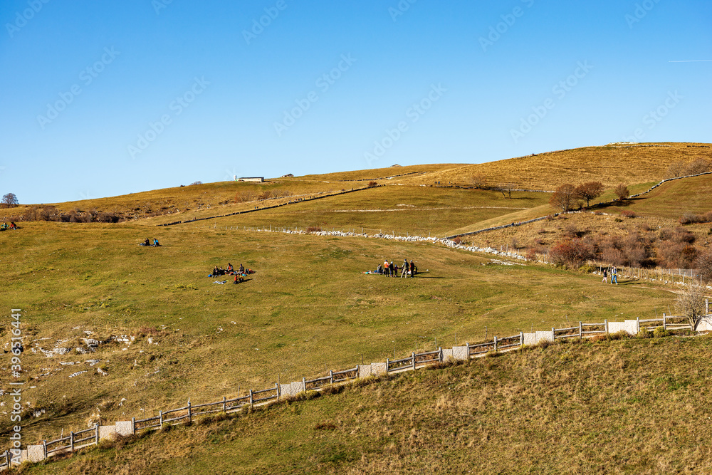 Group of hikers relax on green meadows on the Lessinia Plateau, Regional Natural Park, Alps, Verona Province, Veneto, Italy, Europe.