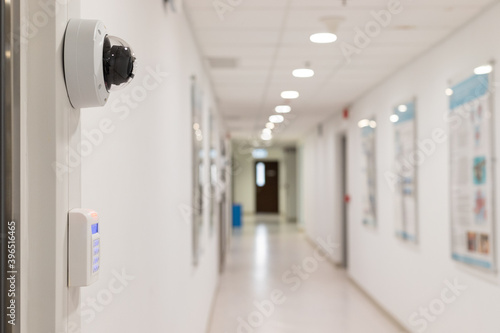 Security surveillance system (camera and digital smart door lock) at the entrance to a modern office building or advanced laboratory with blurred corridor