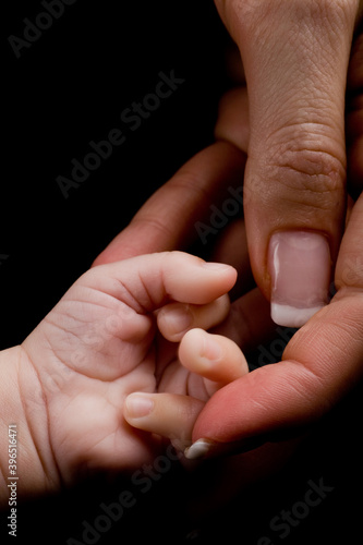 New born holding his or hers mothers hand. Studio photo isolated on black background.