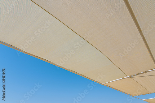Texture of material of sun shades on summer sunny beach isolated at bright blue sky background. Horizontal color photography.