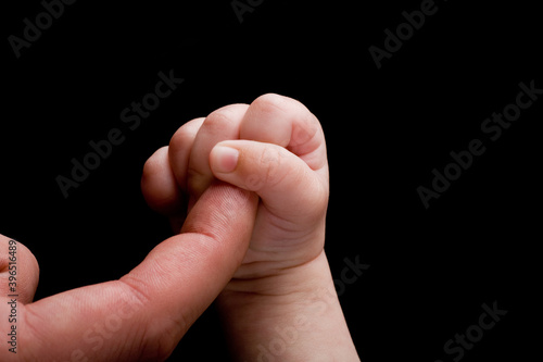 New born holding his or hers mother or fathers finger. Studio photo isolated on black background.