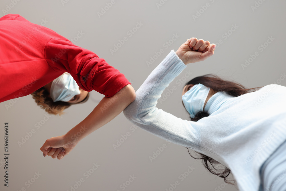 Two women in protective medical masks touching each other with their elbows Two women in protective medical masks touching each other with their elbows