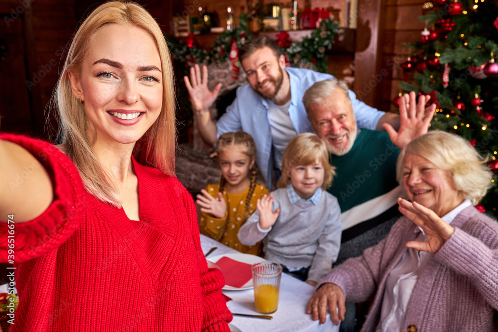 blond woman taking selfie on smartphone with members of family going to celebrate new year or christmas. at home