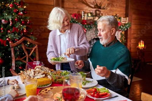 elderly man and woman enjoy celebrating new year together, senior female puts food on plate and talk with gray-haired man