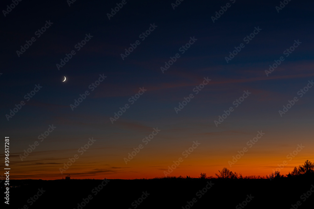 Dusk landscape with the waxing crescent moon over the little town in silhouette.