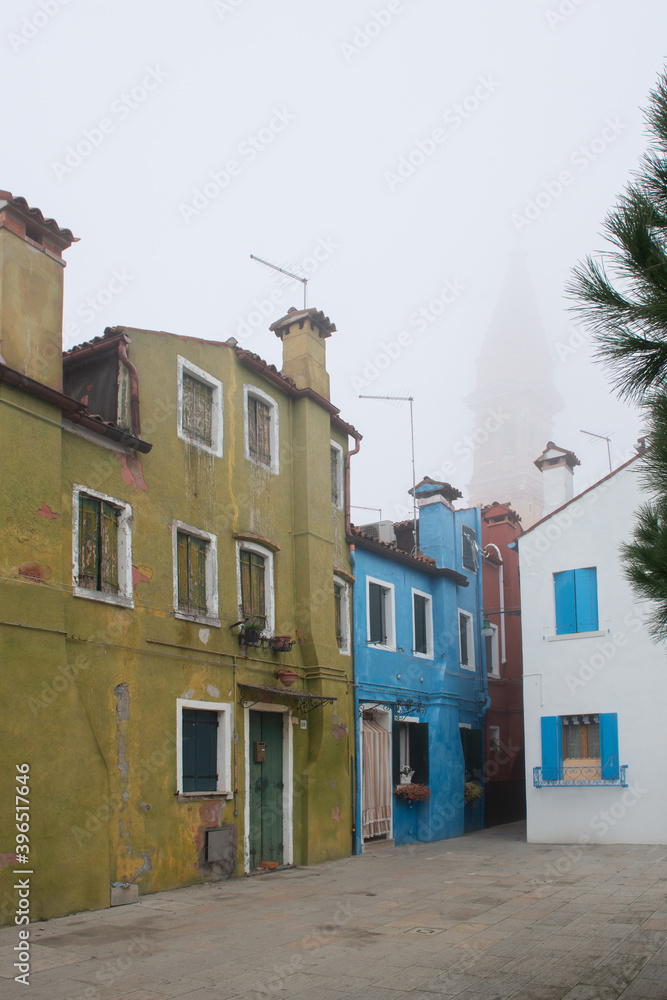Misty picture of street with colored houses in fog, italian island Burano, province of Venice, Italy, foggy weather.