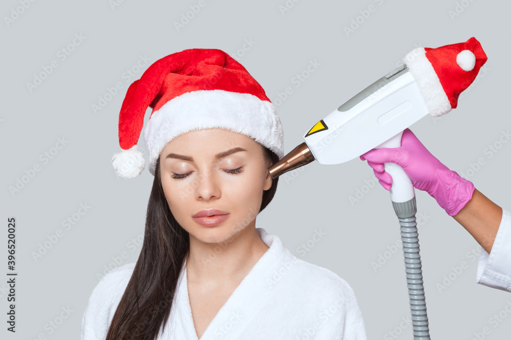 Carbon face peeling procedure in a beauty salon. Girl in santa claus hat. New Year's and Cosmetology concept. Carbon face peeling procedure in a beauty salon. Girl in santa claus hat. New Year's and Cosmetology concept.