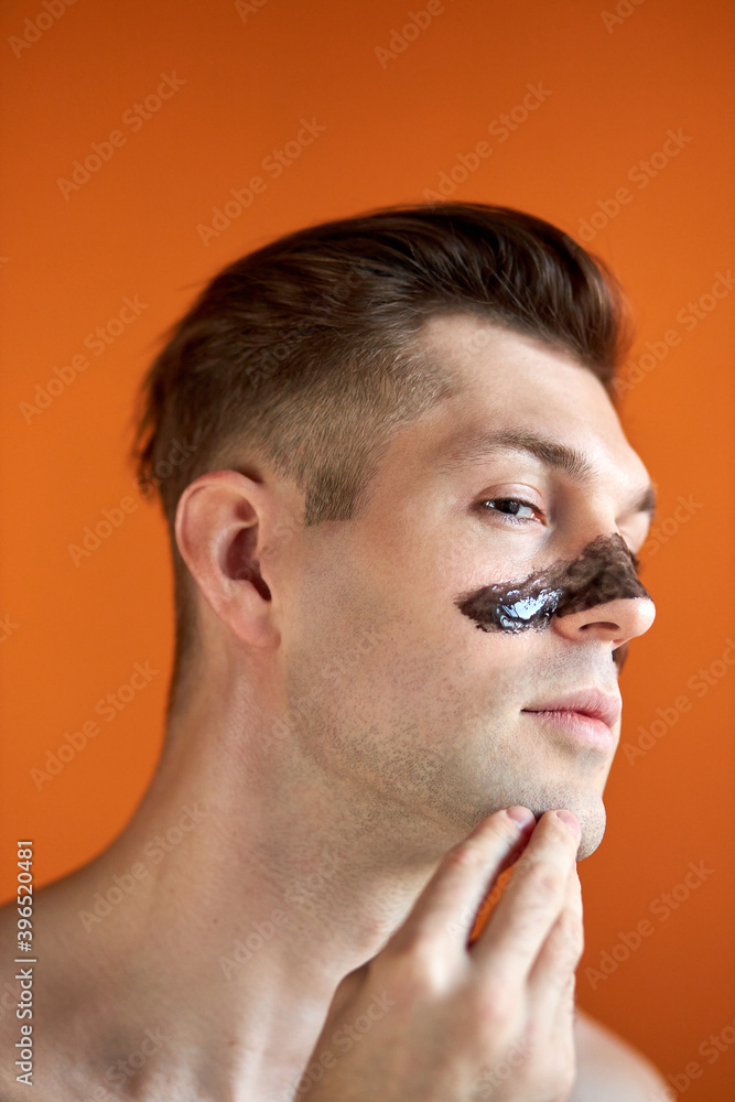 Obraz premium handsome shirtless caucasian guy stand with mask on nose, posing isolated over orange studio background, looking away