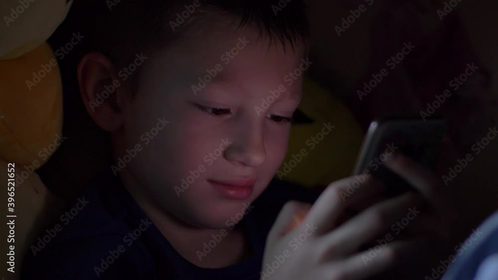 young boy is watching the smartphone in the bed on the night young boy is watching the smartphone in the bed on the night
